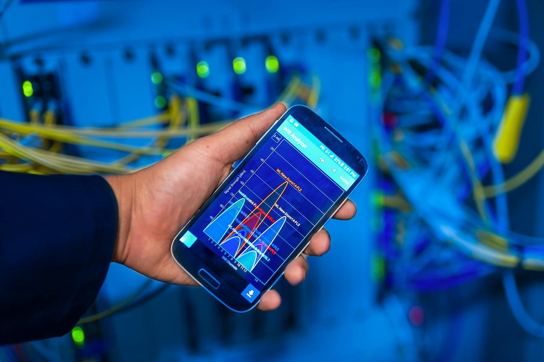 A hand holds a smartphone with a network interface inside a high-tech server room.